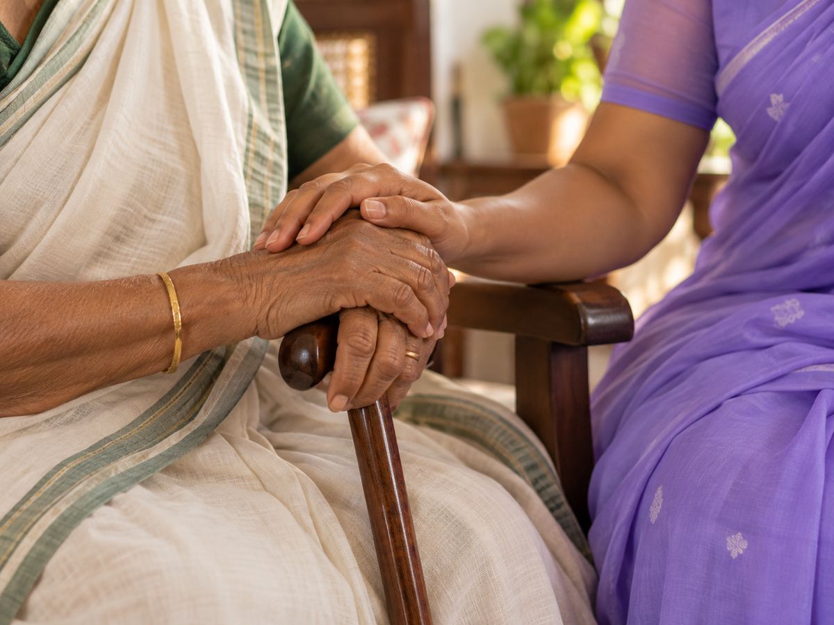 A carer’s hand resting on an elderly woman’s hands