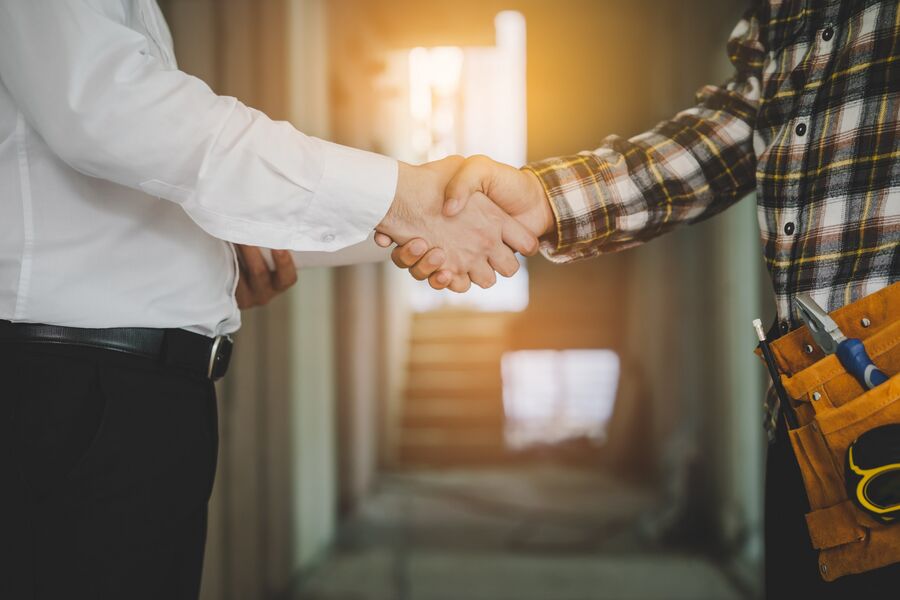 A homeowner shaking hands with a tradesperson wearing a tool belt